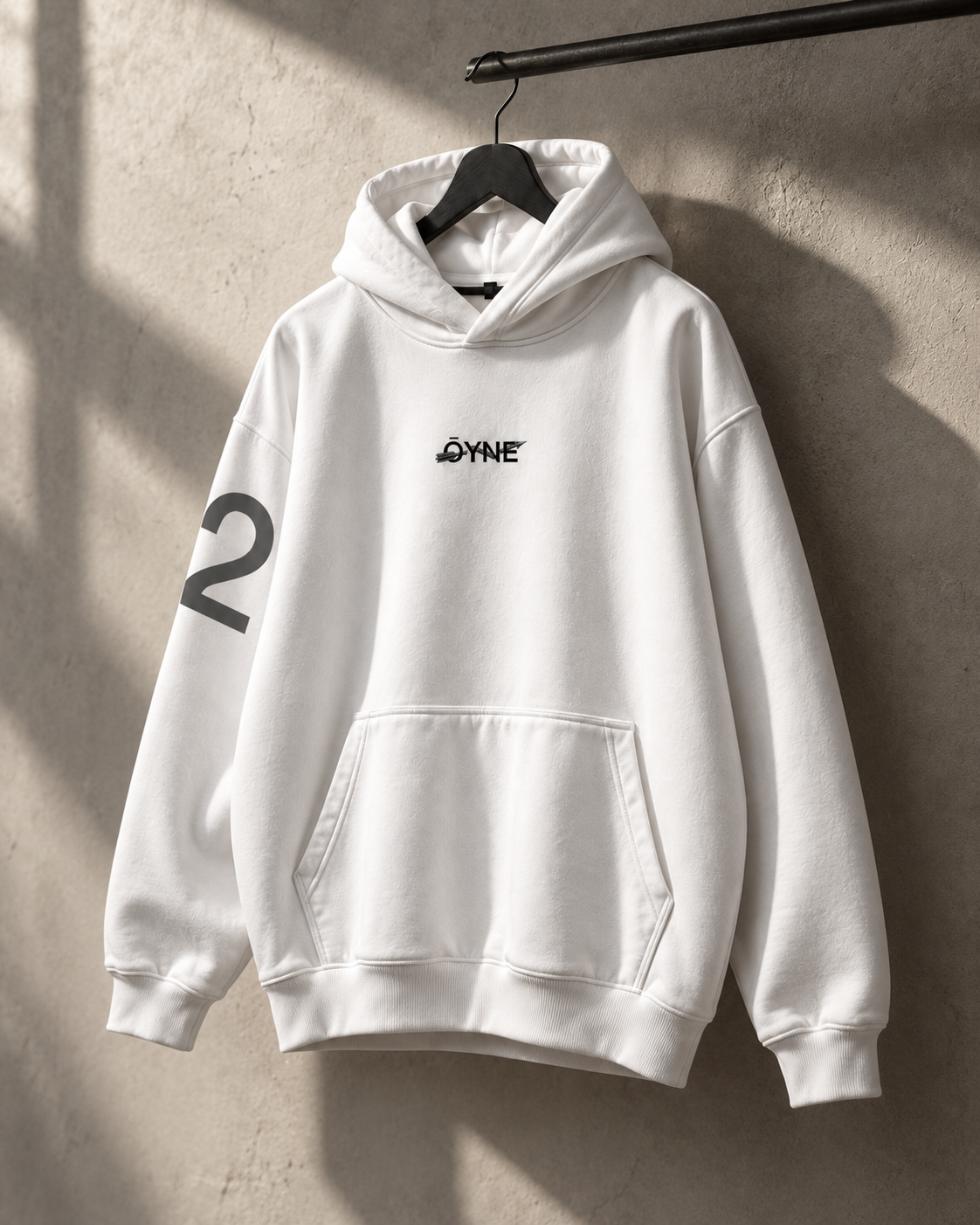 White ŌYNE hoodie on a hanger in a sunlit studio